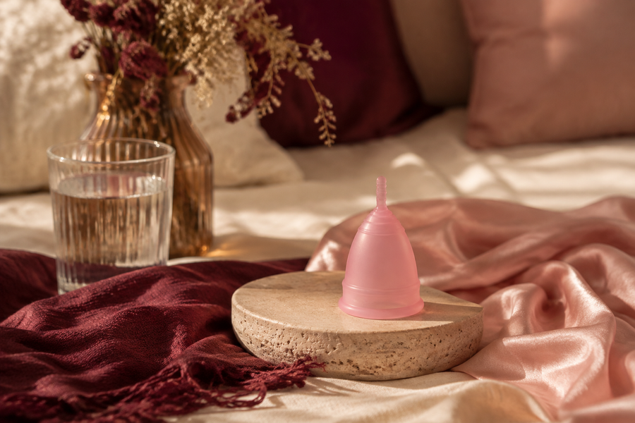 Coupe menstruelle rose présentée dans une ambiance chaleureuse bordeaux et poudrée